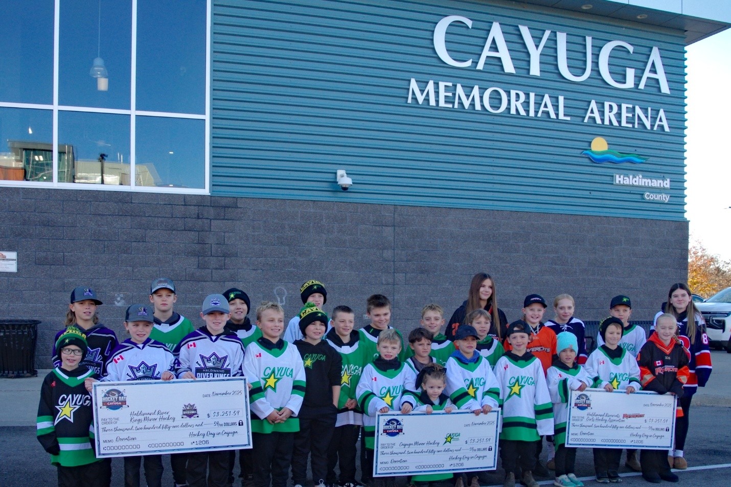 Young hockey players outside Cayuga Memorial Arena with fundraising cheques for local minor hockey